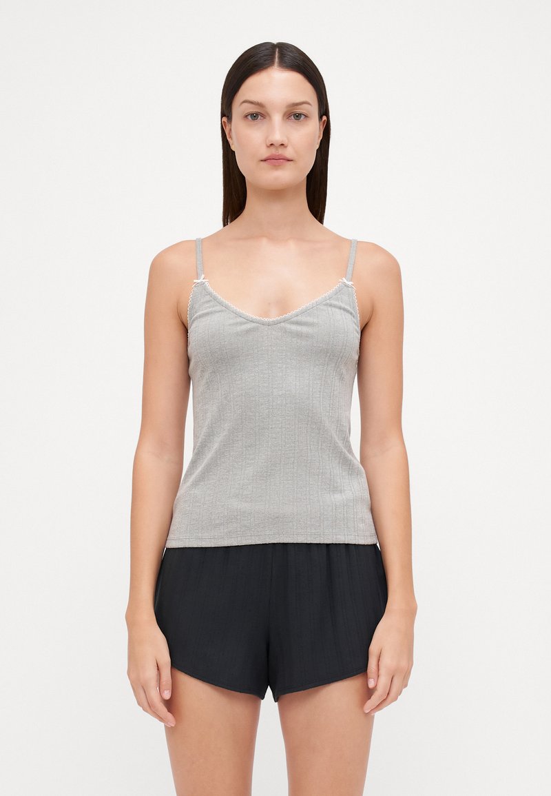 Top en maille grise avec des bretelles fines, présentant un décolleté en V et des bords festonnés. Porté avec un short noir à texture, ample.