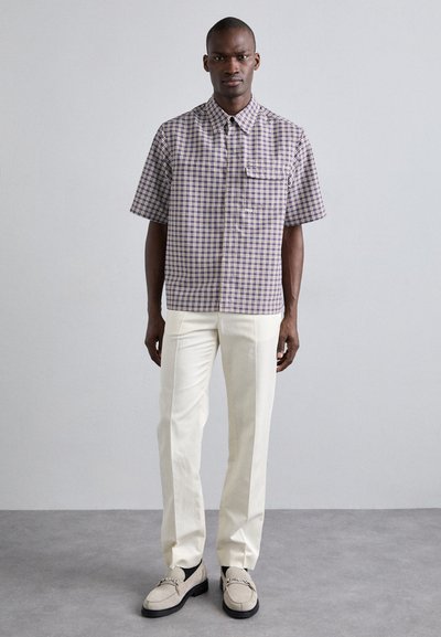 Camisa de cuadros, de manga corta, en morado y blanco, con un bolsillo en el pecho y cuello tipo camisa, combinada con pantalones blancos y mocasines beiges.