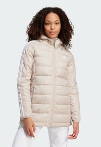 Bež jakna s kapuljačom, sadrži bijele vertikalne pruge duž rukava, zatvaranje na zip, kventan dizajn i suptilni brend na prsima.