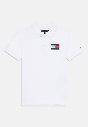 Camisa polo blanca con cuello, tres botones y un parche de logo en azul, rojo y negro en el lado izquierdo del pecho. Mangas cortas.