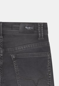 Jeans de mezclilla negra con una textura suave, que cuentan con una etiqueta de logo en la cintura, bolsillos en ángulo y detalles de costura en contraste.