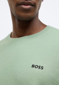 Ανοιχτοπράσινο πλεκτό πουλόβερ με υφή, με στρογγυλή λαιμόκοψη και το λογότυπο "BOSS" σε μαύρη κεντητική στο στήθος. Κοντινή προβολή.