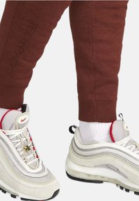 White and grey Nike Air Max 97 sneakers with red accents and reflective detailing, worn with brown tapered sweatpants.
