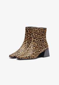 Bottines imprimé léopard en suède, avec un bout pointu et un talon carré. Le design se compose de couleurs marron, noir et beige.