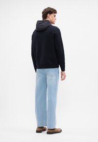 Sweater preto com mangas texturizadas e capuz cinza, combinado com jeans azul claro e botas castanhas. Design simples, tecido suave.