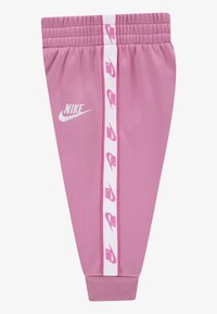 Lyserøde Nike joggebukser med en hvid elastisk talje, der har en hvid stribe ned langs siden med gentagne lyserøde logoer. Blødt stof.