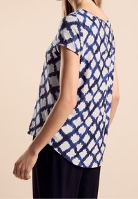 Kortärmad topp i ljusblått och marinblått med ett abstrakt mönster. Har en avslappnad passform och lätt kurvatur vid fållen. Slät textur.