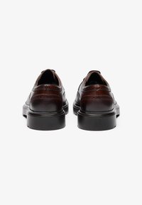 Zapatos de cuero marrón con un acabado suave, que presentan detalles de brogue, una punta redondeada y una suela de goma negra. Diseñados para vestimenta formal.