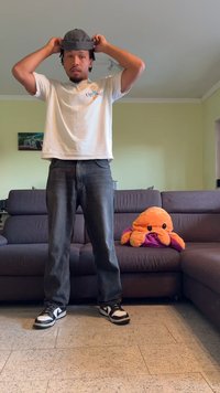 Grijze pet, witte t-shirt met logo, donkere spijkerbroek en zwarte sneakers met witte accenten. Pluchen oranje octopus met paarse details op de bank.