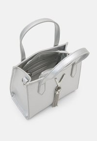 Sac à main en cuir argenté texturé avec deux poignées, une fermeture éclair, des poches intérieures et un pompon en métal décoratif.