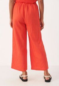 Rode linnen broek met wijdere pijpen en een elastische tailleband, voorzien van een gladde textuur en een losse pasvorm. Gekleed met een tan kleurige sandalen met bandjes.