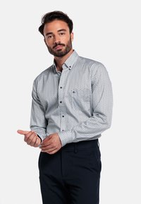 Witte overhemd met een geometrisch marineblauw patroon, lange mouwen en een borstzak. Gecombineerd met een donkere pantalon. Formele uitstraling.