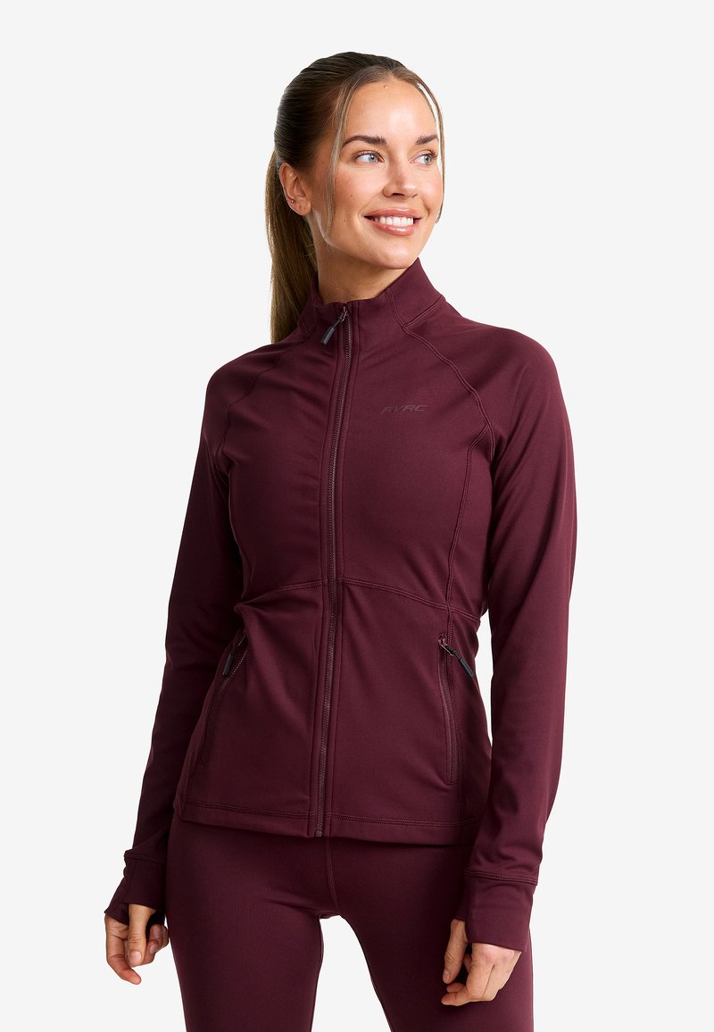 Burgundy idrottsjacka med hög krage, dragkedja framtill och två sidofickor. Tillverkad av flexibelt tyg med figurnära design och långa ärmar.