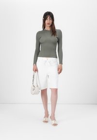 Top a maniche lunghe a coste verde oliva, bermuda bianchi su misura e sandali piatti beige. Gli accessori includono una piccola borsa strutturata.