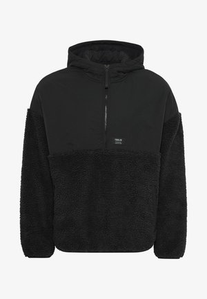Hoodie noir à col zippé, avec un bas en polaire texturée douce, contrastant avec un tissu noir plus lisse au-dessus.
