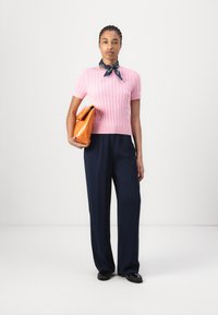 Pull en tricot rose à manches courtes avec un motif texturé, associé à un pantalon large bleu marine. Les accessoires comprennent un sac à main orange et une écharpe bleue.