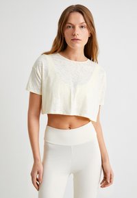 Afkortet, kortærmet top i en cremet gul farve med et subtilt tekstureret mønster. Sat sammen med højtaljede, tætsiddende hvide leggings.
