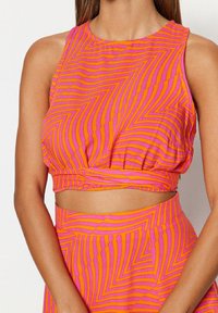 Top court rayé rose et orange avec un col arrondi et un ourlet élastique, présentant un motif ondulé et des détails de tissu froncé.