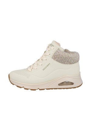 Zapatilla alta en crema con un cuello de punto texturizado. Cuenta con una punta perforada y una suela acolchada con una unidad de aire visible.