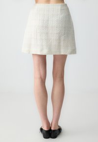 Une courte jupe en tweed blanche avec une finition texturée et un design évasé, associée à des chaussures noires à enfiler avec des accents dorés.