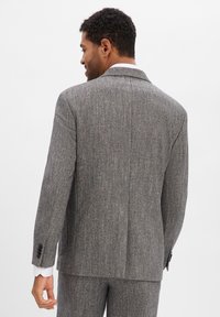 Szara marynarka w jodełkę z klapami z wycięciami, dopasowanym krojem i pojedynczym rozcięciem z tyłu. Posiada mankiety zapinane na cztery guziki oraz teksturowaną tkaninę.