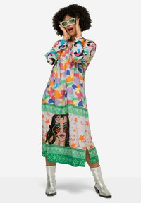 Farbiger langer Kleid mit geometrischen Mustern in Rosa-, Blau- und Grüntönen. Verfügt über einen grünen gemusterten Saum und einen Grafikdruck eines Frauengesichts.