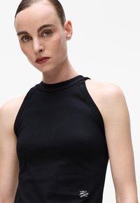 Black sleeveless top with a high neckline featuring a textured sparkly accent. Smooth fabric with a fitted silhouette and small logo detail.