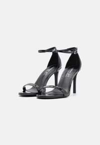 Mustat patenttikiiltoiset korkokengät, joissa on nilkkahihna, avonainen kärki ja hoikka stiletto-korko. Kiiltävällä pinnalla.