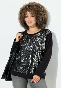 Felpa nera con maniche lunghe, caratterizzata da un davanti impreziosito da paillettes. Tessuto morbido con una vestibilità comoda, abbinata a pantaloni grigi e una borsa nera.