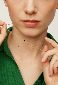 Collar de oro con un pequeño colgante que presenta un diseño texturizado y un acento de piedra negra, llevado por un modelo que sostiene la cadena.