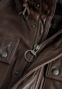 Braune Lederjacke mit sichtbarem Reißverschluss und rundem Ziehgriff, Druckknöpfen und kariertem Innenfutter. Strukturfähiger Oberflächen mit Steppdetails.