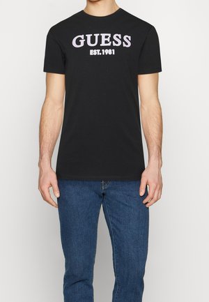 Zwarte katoenen T-shirt met gedurfde 'GUESS'-tekst en 'EST. 1981' in wit en paars. Eenvoudig, casual ontwerp met een ronde halslijn.