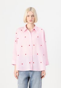 Ανοιχτό ροζ πουκάμισο με κόκκινο κεντημένο σχέδιο καρδιάς. Διαθέτει γιακά και μακριά, αναδιπλωμένα μανίκια. Χαλαρός σχεδιασμός με άνετη εφαρμογή.