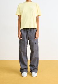 T-shirt en coton jaune avec col rond et manches courtes, associé à un pantalon cargo gris ample avec poches latérales et taille à cordon.