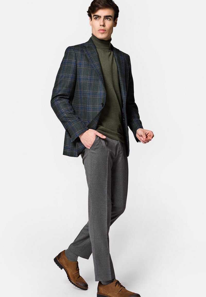 Marynarka w niebiesko-zielony wzór kraty, zestawiona z ciemnozielonym golfem i szarymi spodniami o dopasowanym kroju. Brązowe sznurowane botki dopełniają wygląd.