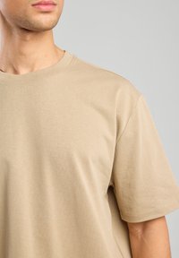 Maglietta in cotone beige con scollatura rotonda e maniche corte, caratterizzata da una superficie liscia e dettagli di cucitura minimi.