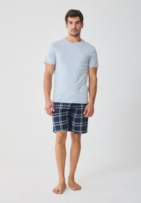 Light blue cotton t-shirt with a round neckline and small yellow logo. Navy plaid shorts with white lines, knee-length and lightweight.
