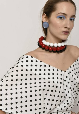 Top de lunares en blanco y negro, sin hombros, con un acabado brillante, combinado con un collar de cuentas grandes multicolores y pendientes azules grandes.