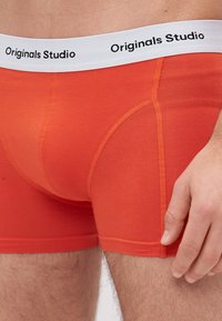 Oranžové bavlněné Boxerky s bílým elastickým pasem, na kterém je černě vytištěno "Originals Studio". Hladký povrch a přiléhavý střih.