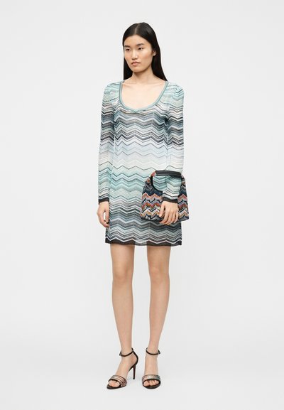 Μίνι φόρεμα με στρογγυλή λαιμόκοψη σε κυματιστό μοτίβο με αποχρώσεις μπλε, γκρι και μαύρου. Συνδυάζεται με πολύχρωμη τσάντα με σχέδιο και πέδιλα με λουράκια.
