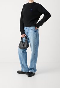 Pull noir côtelé, jean large bleu clair, sac à main noir avec ferrures argentées, et mocassins noirs. Tenue décontractée en couches.