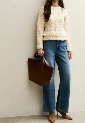 Femme portant un pull crème en maille torsadée avec franges, jean bleu jean large, talons pointus beige, tenant un grand sac fourre-tout en cuir marron.