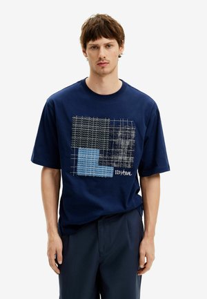 Snavyblå t-shirt i bomuld med et grafisk print i sorte og blå firkanter. Kortærmet og afslappet pasform. Designet inkluderer lagdelte teksturer.