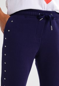Navy blue sweatpants made of soft fabric, featuring a drawstring waist and decorative silver studs along the outer seam.