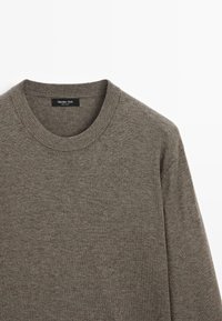 Šedý pletený svetr s kulatým výstřihem a žebrovanými detaily na límci. Měkká textura a minimalistický design. Viditelné štítko značky uvnitř.