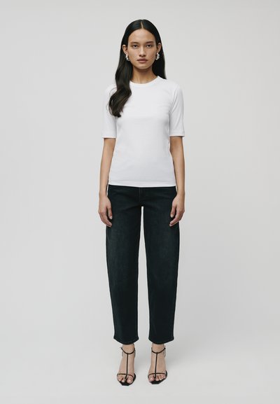Witte korte mouwen t-shirt gecombineerd met donkere hoge taille spijkerbroek. Model draagt zwarte sandalen met bandjes en grote zilveren oorbellen. Eenvoudig ontwerp, gladde textuur.