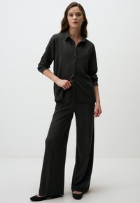 Ensemble de détente noir à côtes verticales comprenant une chemise à col avec des boutons et un pantalon large, complété par des ballerines noires. Texture lisse.