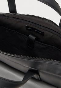 Black leather tote bag with zipper closure. Interior features a black fabric lining, an organizational pocket, and a logo label.