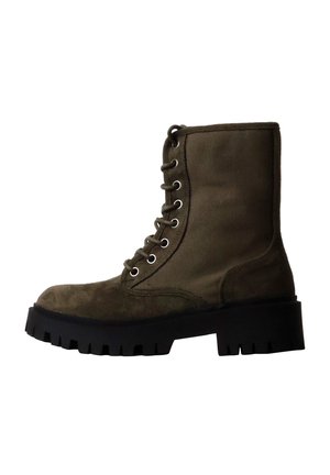 Botte haute à lacets vert foncé avec semelle noire épaisse à crampons et œillets pour lacets sur fond blanc.