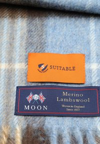 Merinolamswolstof in blauw- en beigetinten met labels: oranje "Suitable" en marineblauw "Moon" met accenten van de Britse vlag.